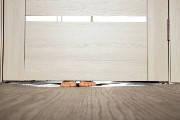 The girl's legs sticking out from under the door with a depression in the floor in the apartment, standing behind the door, legs under the door
