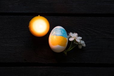 Paskalya yumurtası Ukrayna bayrağı, mum ve çiçek açan kiraz dallarıyla koyu ahşap masa ve yanan mum, Ukrayna 'da Paskalya Bayramı