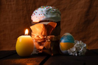 Ukrayna bayraklı Paskalya yumurtası, çiçek açan kiraz dalı ve şenlikli Paskalya pastası ve mum evdeki ahşap masada, karanlıkta, Ukrayna 'da Paskalya Bayramı