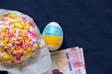 Paskalya pastası ve 200 hryvnia faturası ve mavi arka planda Ukrayna bayrağı olan bir yumurta, Paskalya masrafları, harcamalar ve para.