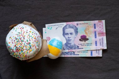Paskalya pastası ve 200 Hryvnia faturası ve gri arka planda Ukrayna bayrağı olan bir yumurta Paskalya harcamaları, harcamalar ve para.