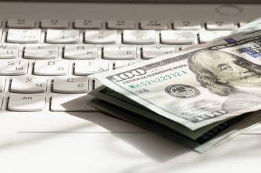 Yüz dolarlık banknotlar beyaz bir dizüstü bilgisayarın klavyesinde, dijital kazançlar, çevrimiçi çeviri, iş ve kâr üzerine kuruludur.