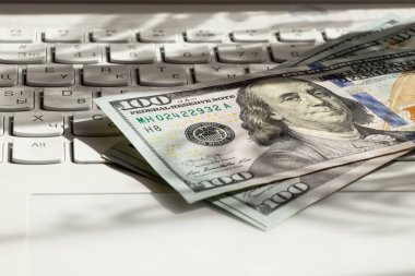 Yüz dolarlık banknotlar beyaz bir dizüstü bilgisayarın klavyesinde, dijital kazançlar, çevrimiçi çeviri, iş ve kâr üzerine kuruludur.