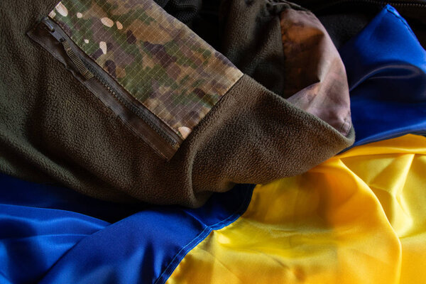 Warm camouflage uniform of Ukrainian soldier lies on Ukrainian flag, soldier uniform in Ukraine