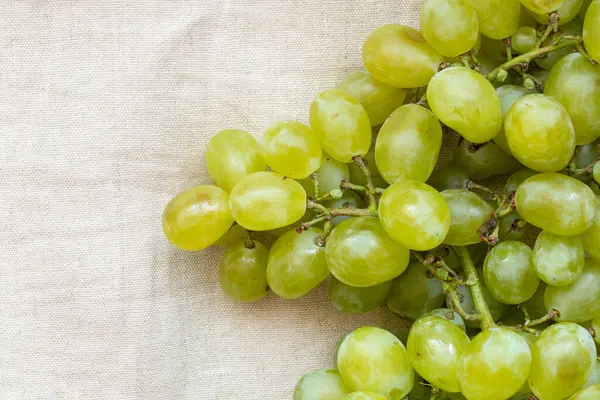 Açık bej kumaş ve meyvelerde bir demet yeşil üzüm var.
