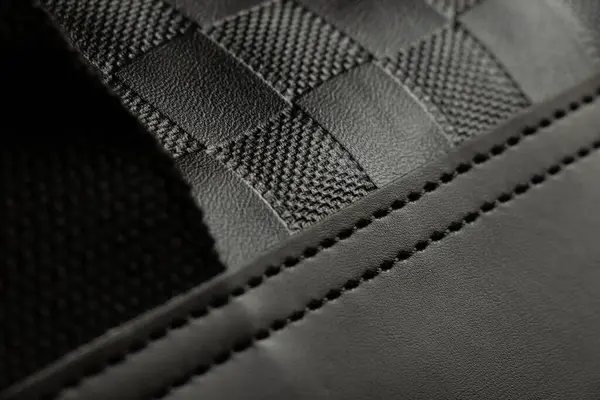 Siyah erkek çantasına kabartma ve dikişli yapay deri dokusu, yakın plan, siyah arka plan.