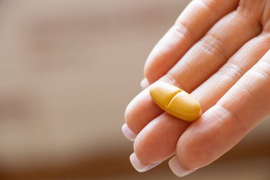 Tarafsız arka plan, sağlık, tedavi ve vitamin alan bir kadının elindeki sarı tablet