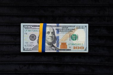 Siyah arka plan, finans ve işletme üzerinde Ukrayna bayrağı renginde kurdele olan dolar yığını