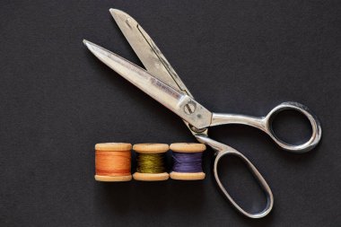 Terzi makası ve siyah arkaplan üzerinde ahşap iplik makaraları, dikiş ve kesme araçları