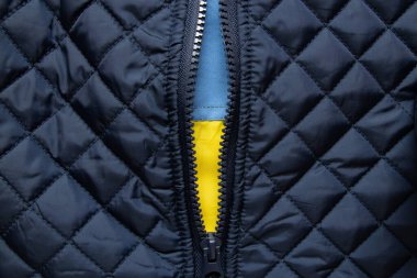 Mavi örtülü ceketin fermuarının altında Ukrayna bayrağı, metanetin ve milli gururun sembolü.