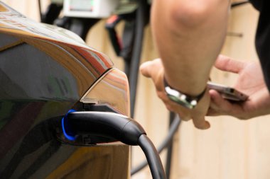 Ukrayna Dnipro 05 / 28 / 2025 - Tesla elektrikli otomobili hızlı şarj, elektrik dolum istasyonunda kablo bağlantısı ve yakınlarda telefonu olan bir adam