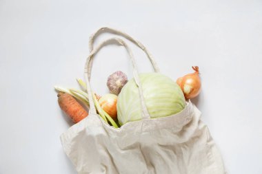 Sebzeli eko-çanta: lahana, havuç, soğan ve sarımsak beyaz arka planda, vejetaryenler için market seti ve sağlıklı beslenme