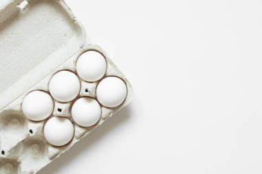Beyaz arka planda karton bir kutuda beyaz tavuk yumurtaları.