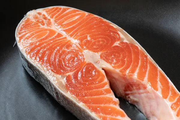 Bir parça çiğ somon siyah bir tabakta uzanıyor.