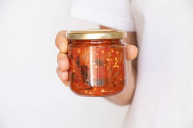 Cam bir kavanozda ev yapımı Adjika, beyaz arka planda altın kapaklı, konserve acı sos ve baharat.