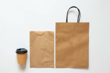 Kağıt torbalar ve beyaz arka planda kapaklı kahve fincanı, kahve ve yiyecek için ambalaj modeli, üst manzara.