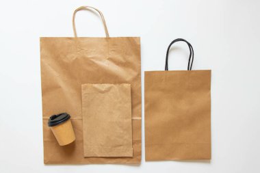 Kağıt torbalar ve beyaz arka planda kapaklı kahve fincanı, kahve ve yiyecek için ambalaj modeli, üst manzara.