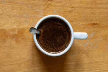 Bir fincan köpüklü sade kahve ve tahta bir masada beyaz bir kaşık, üst manzara, enerji için bir sabah içkisi ve güne bir başlangıç.