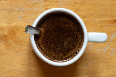 Bir fincan köpüklü sade kahve ve tahta bir masada beyaz bir kaşık, üst manzara, enerji için bir sabah içkisi ve güne bir başlangıç.