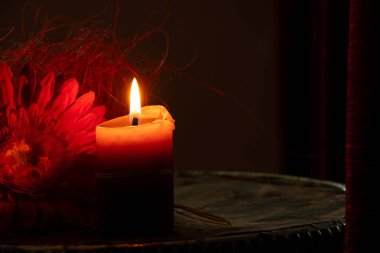Koyu arkaplanda kırmızı çiçeğin yanında yanan mum, anıların sembolü, keder, yas, inanç ve meditasyon.