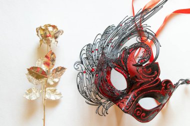 Beyaz tüylü kırmızı karnaval maskesi ve yanında beyaz arka planda altın gül, maskeli balo için dekoratif aksesuar.