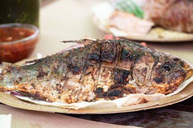 Kızarmış nehir balığı ızgarada, kağıt tabakta soğan ve otlarla birlikte, öğle yemeği.