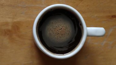 Kahvenin kıvrımları beyaz bardakta, ahşap masanın üstünde, sabah kahvesi