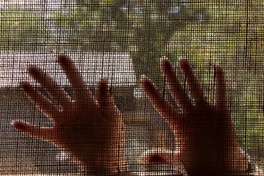 Kadın elleri hafif kumaşa karşı ışıkta ağ desenli, sokakta avuçlar kumaştan geçiyor.