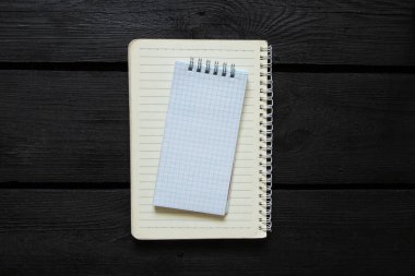 Üzerinde beyaz kareli defter olan dizüstü bilgisayarı aç, hem spiral, hem siyah tahta zemin üzerinde uzanan, hem de üst görünümde, notlar için şablon