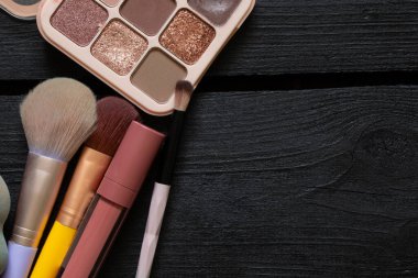 Kozmetik fırçalar, sünger ve göz farı, ruj ve saç düzleştirici siyah ahşap arka plan ve üst görünüm, bakım ve makyaj malzemeleri