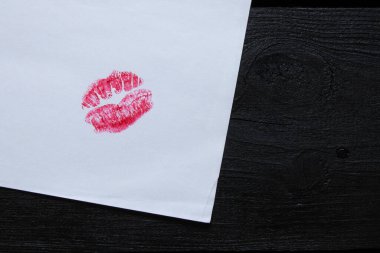 Beyaz kağıda kırmızı ruj sürülmüş parlak dudak izi. Tahta masa üzerinde. Öpüşme ve romantizmin sembolü.