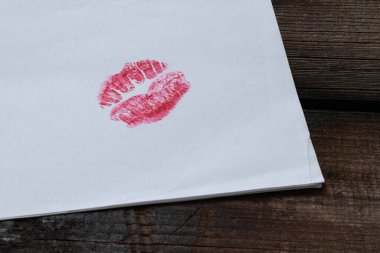 Beyaz kağıda kırmızı ruj sürülmüş parlak dudak izi. Tahta masa üzerinde. Öpüşme ve romantizmin sembolü.