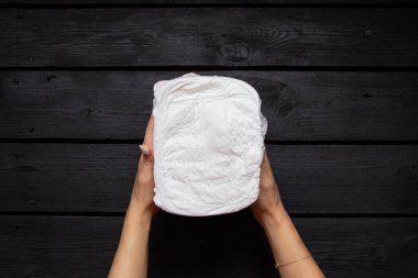 Siyah ahşap arka planda tek kullanımlık beyaz bebek bezi tutan kadın elleri.