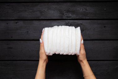 Siyah ahşap arka planda tek kullanımlık beyaz bebek bezi tutan kadın elleri.