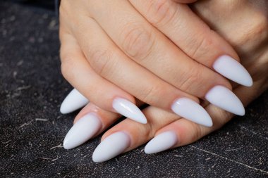 Siyah arka planda uzun, keskin beyaz manikürlü kadın elleri.