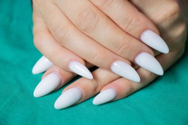 Yeşil kumaşta uzun, keskin beyaz manikürlü kadın elleri.