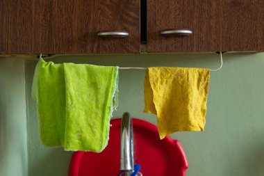 İki mutfak bezi, yeşil ve sarı, bir dairenin mutfağındaki ahşap dolabın altında, lavabonun üstünde bir ipe asılmış.