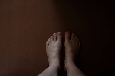 Kadın çıplak ayakla kahverengi zeminde, yarı karanlıkta dairede ve tepeden aşağı manzaralı.