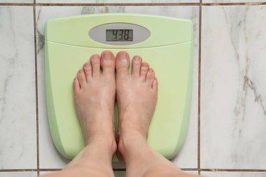 Beyaz fayans, ağırlık kontrolü ve diyet konsepti üzerinde 43 ve 8 kg gösteren yeşil elektronik terazilerde çıplak ayaklar.