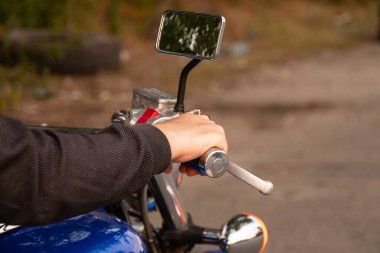 Yazın krom kabzalı ve dışarıdaki kontrol panelinde kırmızı düğmeli motosiklet gidonu tutan erkek el, kontrol kısımları görünür.