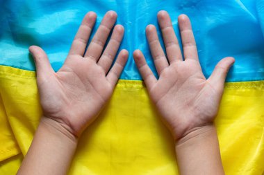 Ukrayna bayrağının arka planında uzanan küçük bir çocuğun avuçlarının içi çocukluğun, barışın, geleceğin ve ulusal kimliğin sembolü olarak açık.