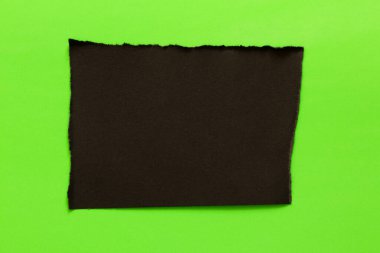 Sivri uçlu ve yırtık kenarlı siyah bir kağıt yaprağı yeşil bir arkaplanda metin ve tasarım için bir şablon ya da yer olarak bulunur