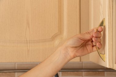 Kadın elleri mutfak dolabının kapısını açıyor. Ahşap bir dokusu ve altın sapı var. Ev hayatı.