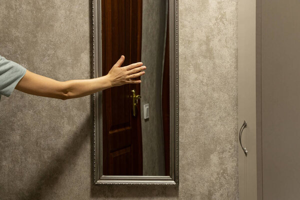 Mirror in the hallway with a closet, reflecting a wooden door and a woman s hand touching the mirror