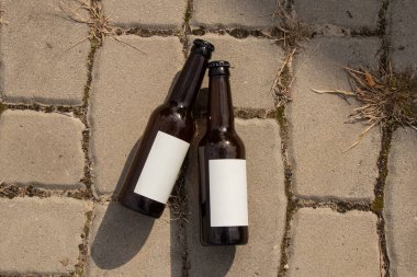 İçecekler, bira veya alkolsüz içecek etiketi tasarımı için taş kaldırım taşlarının üzerinde duran iki beyaz etiketli cam şişe.