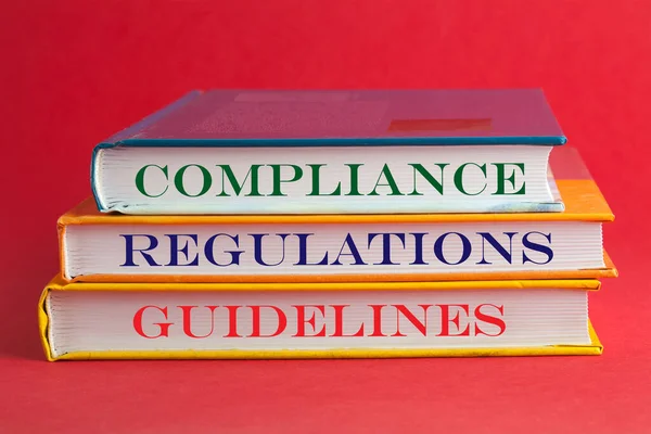 Books with words compliance, regulations and guidelines on red background.
