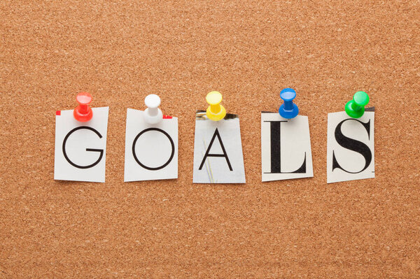 Word goals spelled with black cut out letters from newspaper or magazine pinned on cork board. 