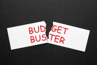 The words Budget Buster on torn paper in black background. clipart