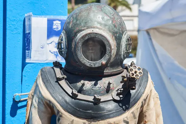 Eski bir dalış kıyafeti canlı deniz eserleriyle çevrili bir sahil sergisinde belirgin bir şekilde duruyor. Kıyafet, açık gökyüzündeki ilk sualtı keşiflerini gösteriyor..