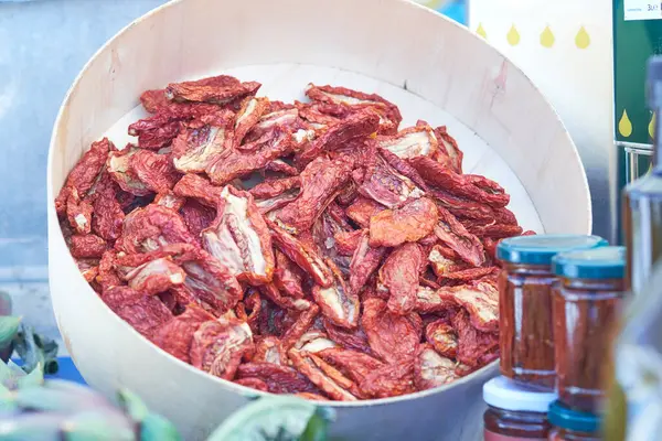 Çiftçi pazarında güneşte kurutulmuş domatesler ahşap bir kasede üst üste yığılır. Canlı renkler ve zengin dokular taze üretimin özünü yakalayan davetkar bir görüntü oluşturur..